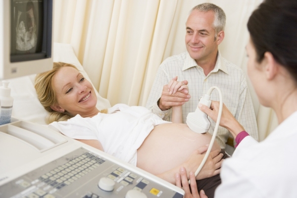 Pregnant woman getting ultrasound from doctor with husband watch